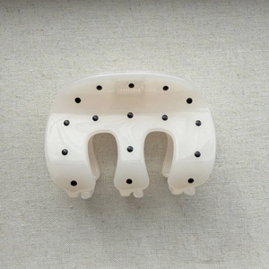 Detailed top view of cream hair claw clip with black polka dots on grey fabric