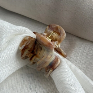 Detail of a large amber marble ink pattern hair claw clip on soft beige linen fabric