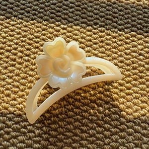 Detailed close-up of cream pearlescent resin flower hair claw clip on knit fabric