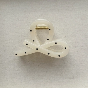 Top view of cream bow hair claw clip with black polka dots and gold metal spring