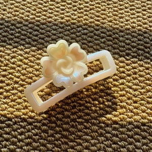 Detail view of pearl-white resin hair claw clip with floral pattern on woven texture