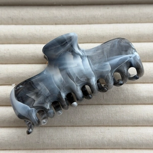 Close-up of a large ink marble hair claw clip on a soft velvet jewelry display tray