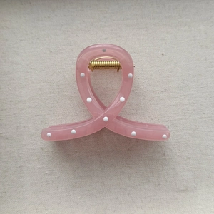 Detailed view of a pink polka dot hair claw clip with golden metal spring and resin finish