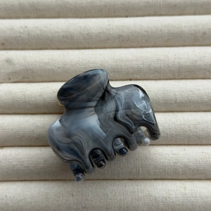 Detail view of large ink-marble hair claw clip with acetate texture on beige fabric