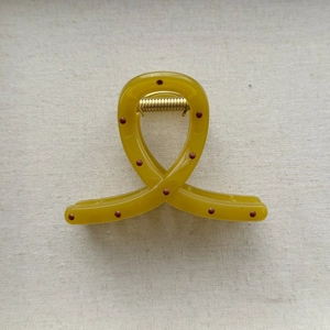 Detail view of mustard yellow polka dot hair claw clip with golden metal spring