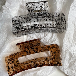 Detailed close-up of large geometric hair claws with grey and amber ink patterns
