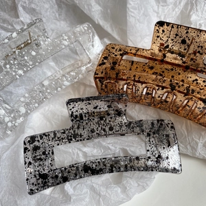 Detailed macro view of three large ink-patterned hair claws on white paper background