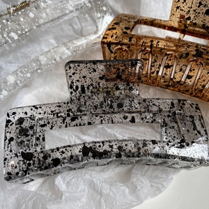 Macro detail of large geometric hair claws with ink splatter design in three colors