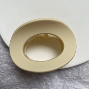 Detail view of oval matte beige hair claw clip with internal grip teeth on grey background