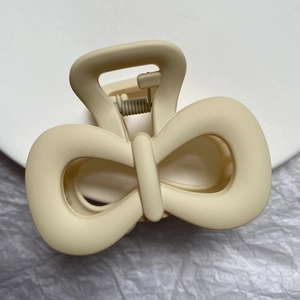 Detail of a matte beige bow-shaped hair claw clip with a durable metal spring