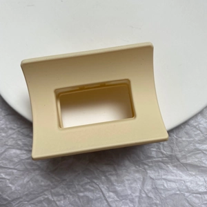 Close-up of cream beige square hair claw clip with matte finish on white textured surface