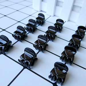 Detail view of 1.5cm black glossy mini hair claw clips set on a clean white tile surface
