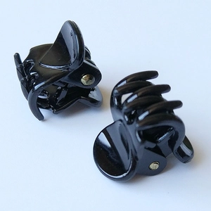 Detail view of two small glossy black plastic hair clips with metal spring hinge