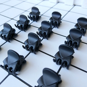 Set of twelve matte black mini claw clips arranged in a grid on a mesh background