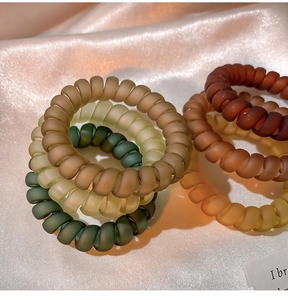Vue détaillée d'élastiques à cheveux spirales mats multicolores sur un tissu satiné rose