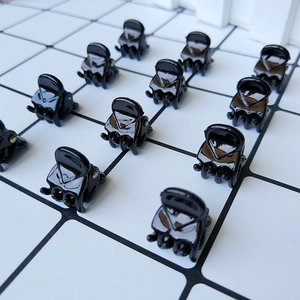 Close-up of small black glossy hair claws arranged on a grid background