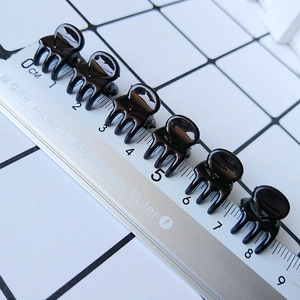 Detail showing set of six mini black resin hair claws measured against a metal ruler