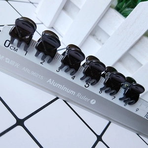 Macro detail of mini 1cm black hair claw clips showing size scale with a ruler