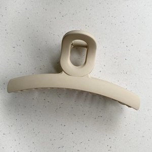 Detailed view of a large matte beige hair claw clip with a textured finish on a white surface