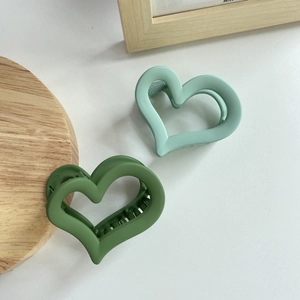 Detail view of two matte green heart-shaped hair claws with hollow design on wooden tray