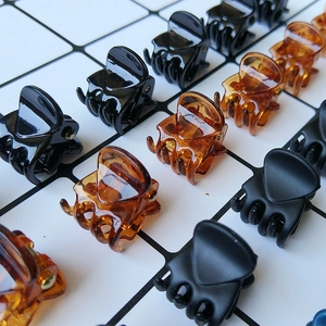 Minimalist 1.5cm mini claw clips in assorted colors like black and amber on a grid background
