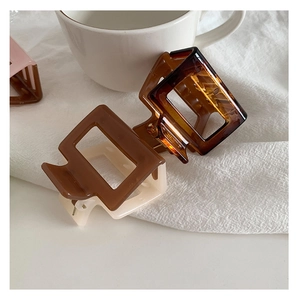 Close-up of geometric square hollow hair claws in brown and cream colors on a white cloth