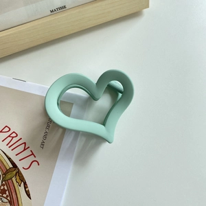 Detail shot of a matte mint green heart-shaped hair claw clip with a secure metal spring