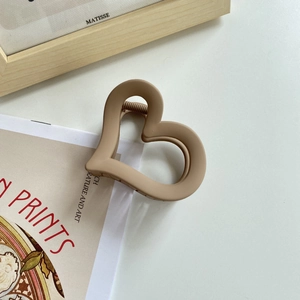 Macro detail of a heart-shaped hair claw clip with a matte beige finish in a minimalist setting