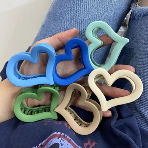 Detailed close-up of colorful heart-shaped matte hair claw clips held in hand