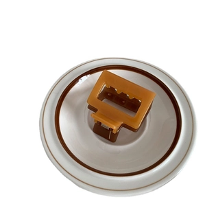 Square amber and dark brown dual-tone resin hair claw clip in a white ceramic dish
