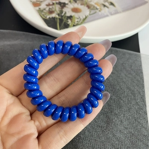 Gros plan sur un élastique à cheveux spirale bleu foncé tenu à la main sur une assiette blanche