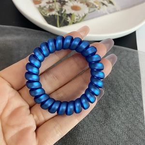 Détail d'un élastique à cheveux spirale bleu foncé mat tenu dans la main d'une personne