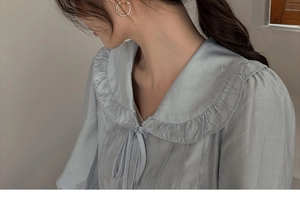 Close-up of light blue satin shirt featuring Peter Pan collar with pleated lace trim