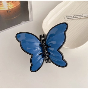 Detailed top view of a royal blue butterfly hair claw clip with black outlines on white ceramic