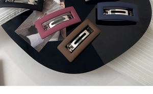 Detail showing four matte minimalist hollow rectangular hair clips on a tray and fabric