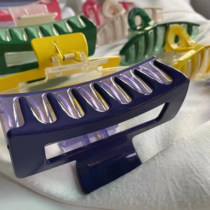 Close-up of a large glossy purple hair claw clip on white fabric with blurred background