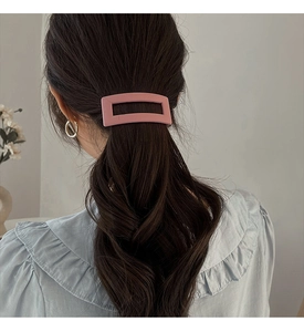 Close-up of matte pink rectangular hair clip styling dark wavy hair in a minimal look