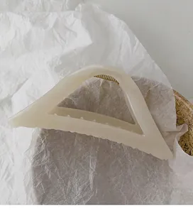 Detailed view of cream geometric hair claw clip with golden spring on aesthetic background