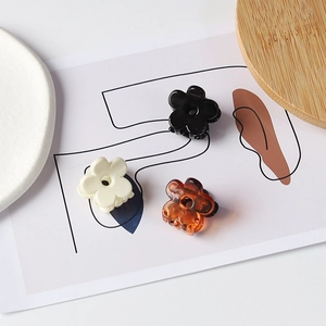 Détail de petites pinces à cheveux fleurs en noir, crème et ambre sur fond blanc