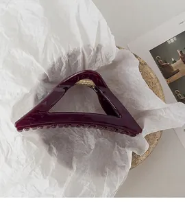 Detail view of burgundy triangular shark clip on minimalist white artistic paper