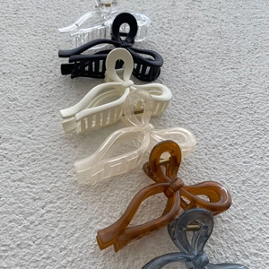 Detail showing assorted color bow-shaped hair claws on a textured minimalist background