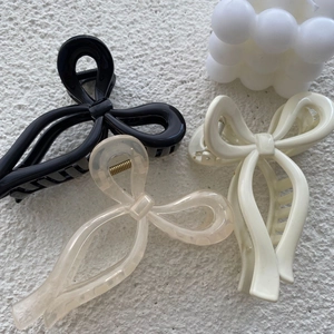 Three bow-shaped hair claw clips in black, cream, and champagne colors on a white surface