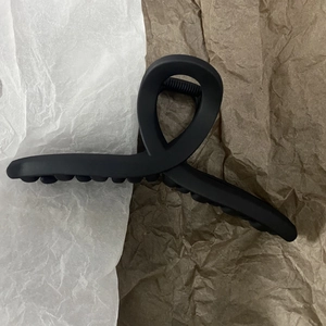 Detail of a 13cm matte black shark hair clip with dense teeth on textured paper