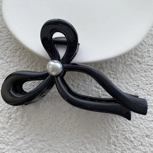 Close-up of black bow hair claw clip with pearl accent and metal spring detail