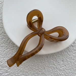 Macro shot of large amber resin bow hair claw clip with golden metal spring detail