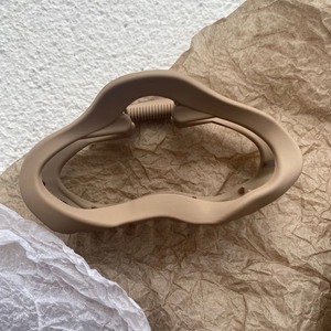 Détail d'une pince à cheveux mate beige ondulée sur un fond de papier kraft texturé
