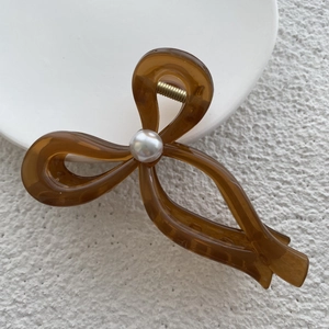 Close-up of translucent brown bow hair claw clip with a white pearl and gold spring detail