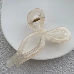 Close-up of translucent cream bow hair claw clip showing golden metal spring detail