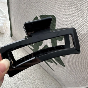 Détail d'une grande pince à cheveux carrée noire brillante tenue sur fond en tissu