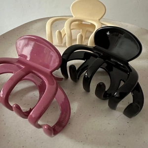Close-up of three glossy hair claws in wine red, black, and beige colors